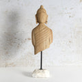 A hand-carved wooden Buddha bust sculpture on a black metal stand with a white marble base.