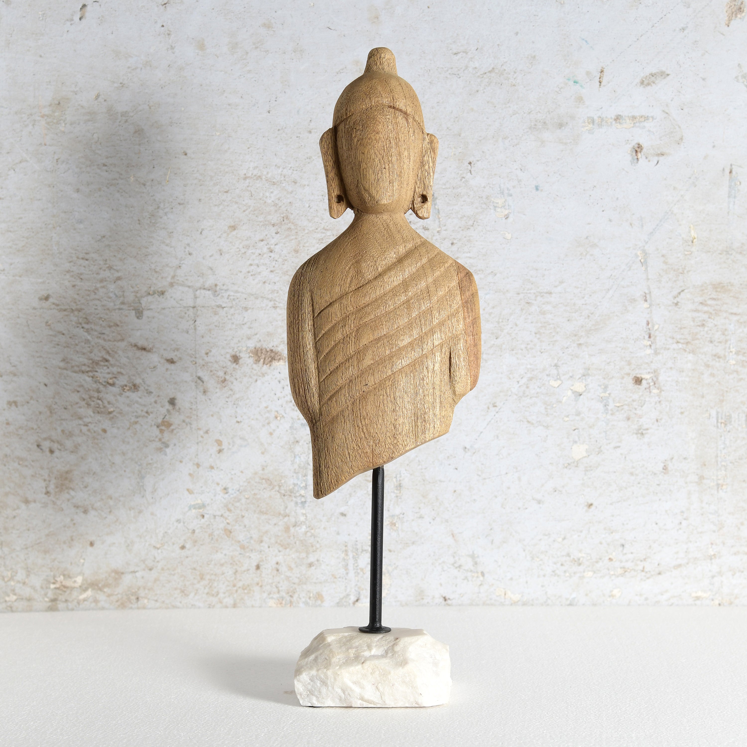 A hand-carved wooden Buddha bust sculpture on a black metal stand with a white marble base.