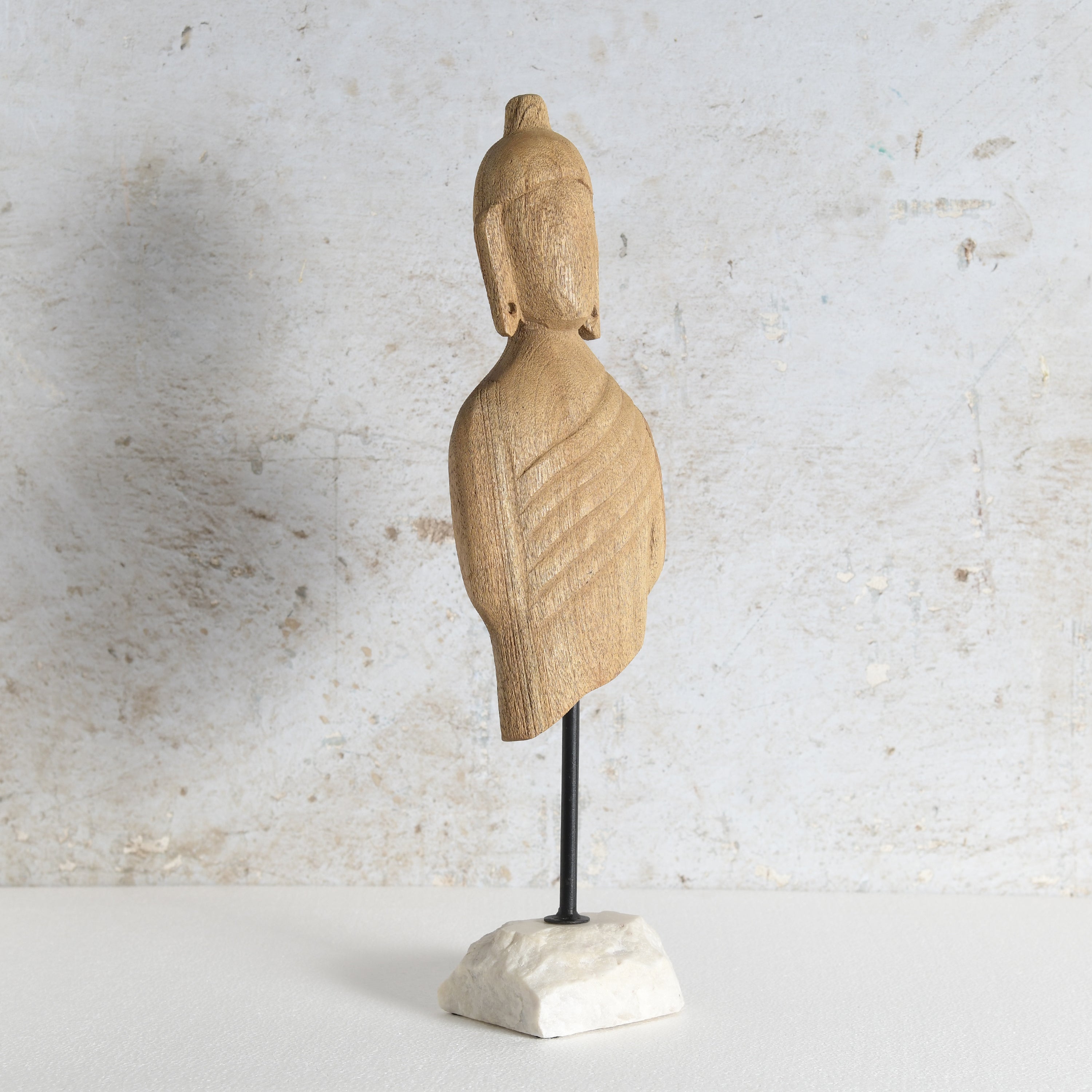 Carved wooden Buddha bust sculpture mounted on a black metal stand with a white marble base.