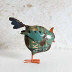 A decorative metal bird sculpture with a distressed teal and brown body, orange beak and legs, and a dark blue tail.