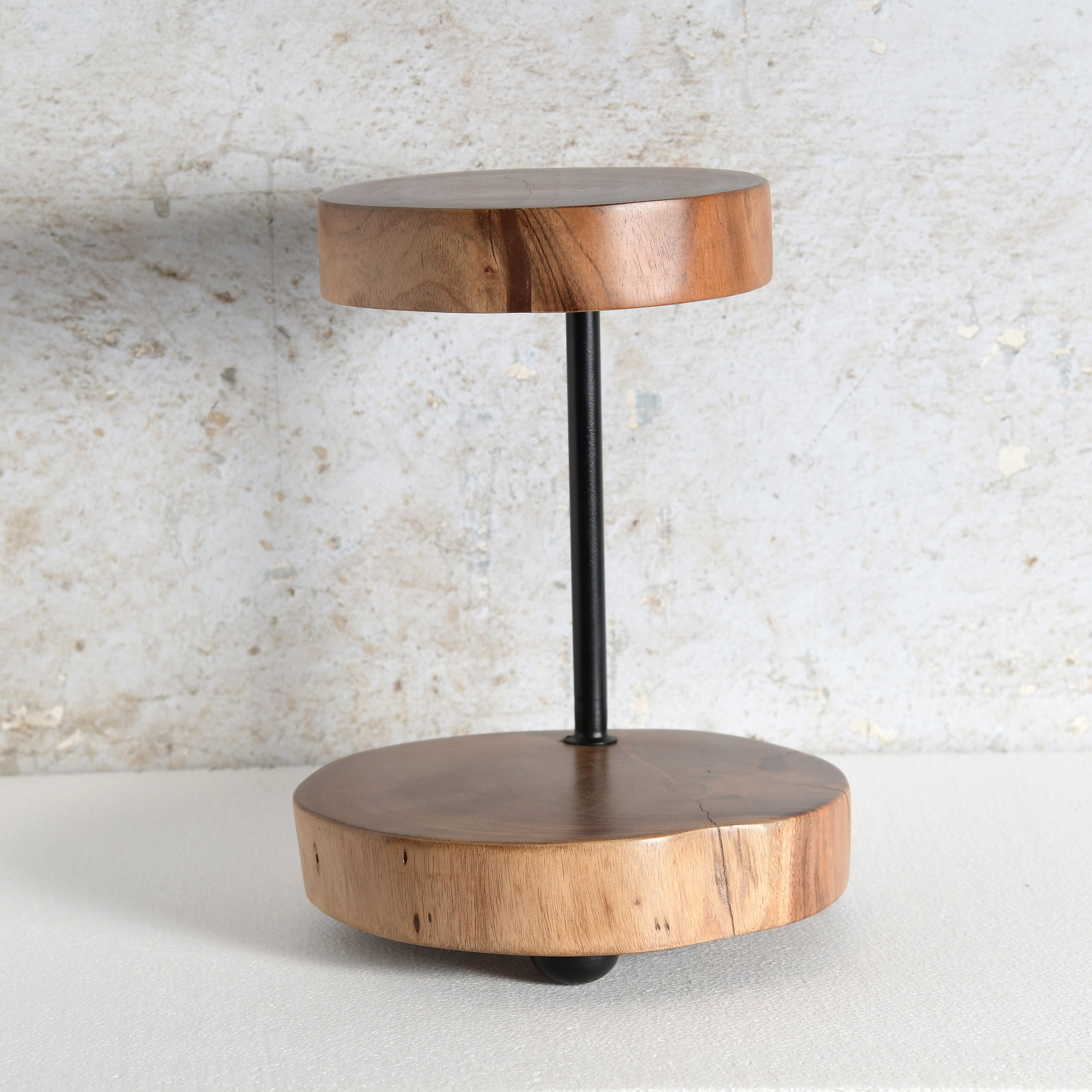 A modern two-tier wooden platter stand featuring circular wood slices at the top and bottom tiers connected by a slim black metal pole.