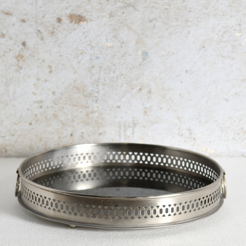A round metal mirror tray with side handles for decorative use.