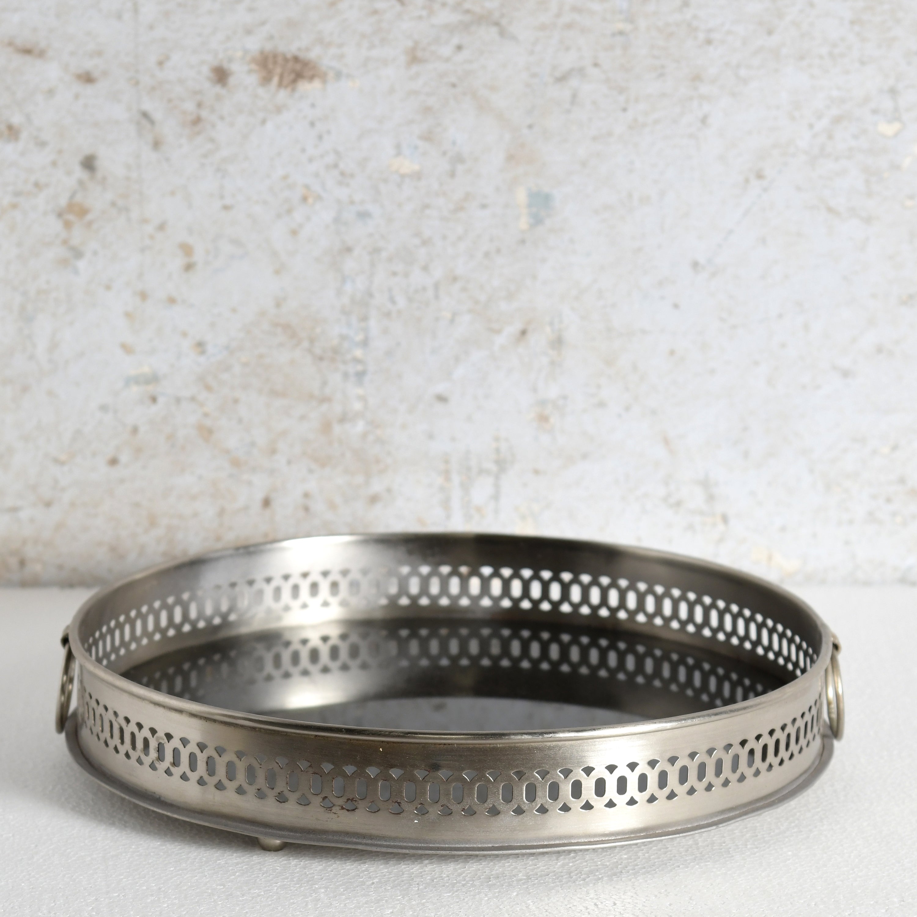 A round metal mirror tray with side handles for decorative use.