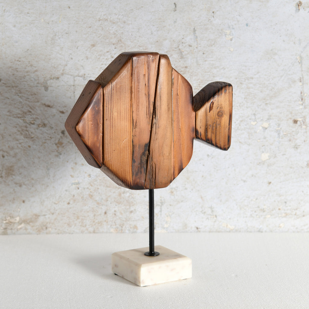 A wooden fish-shaped decorative sculpture mounted on a thin black rod with a square off-white marble base.