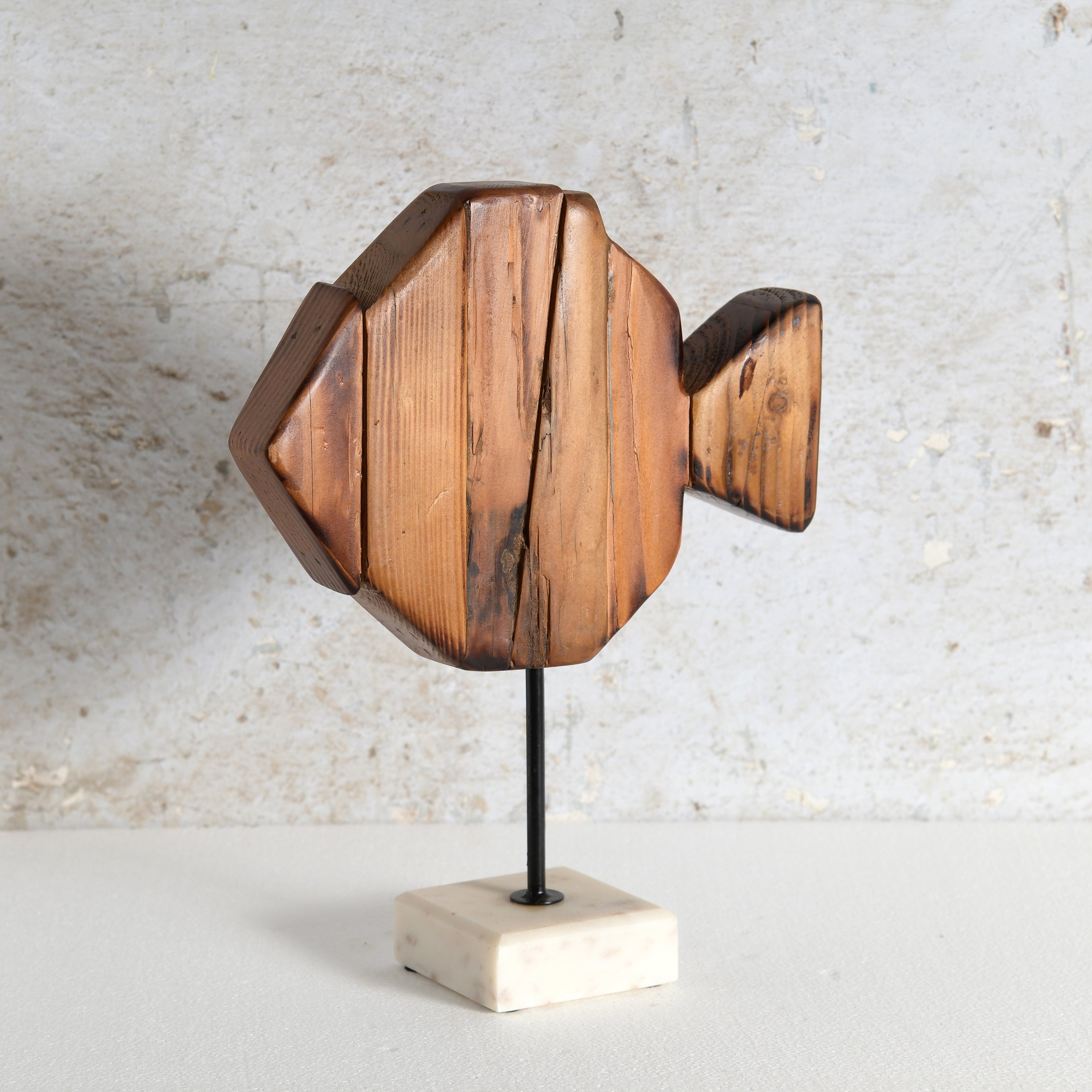 A wooden fish-shaped decorative sculpture mounted on a thin black rod with a square off-white marble base.