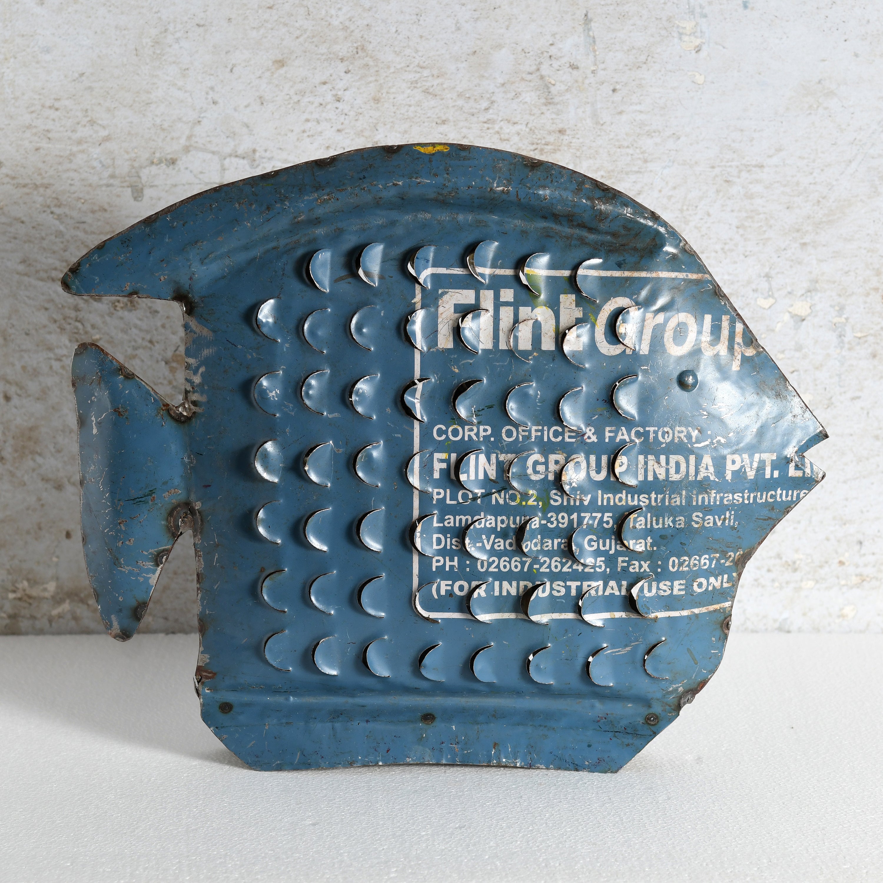 A vintage blue fish-shaped sign with raised circular patterns crafted from recycled metal.