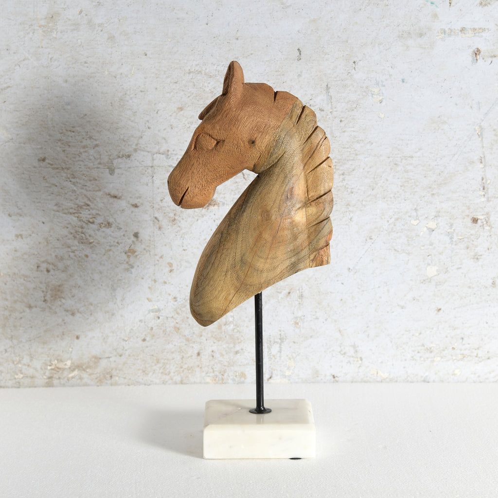 A carved wooden horse head sculpture mounted on a black metal stand with a white marble base.