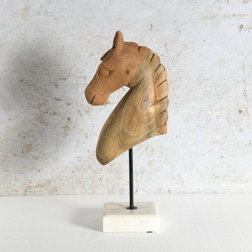 A carved wooden horse head sculpture mounted on a black metal stand with a white marble base.