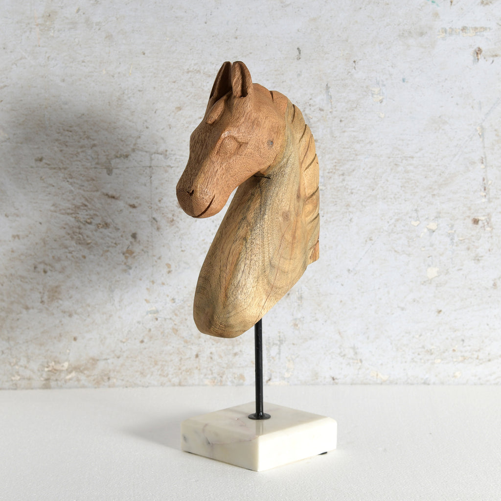 A carved wooden horse head sculpture mounted on a black metal rod over a white marble base.