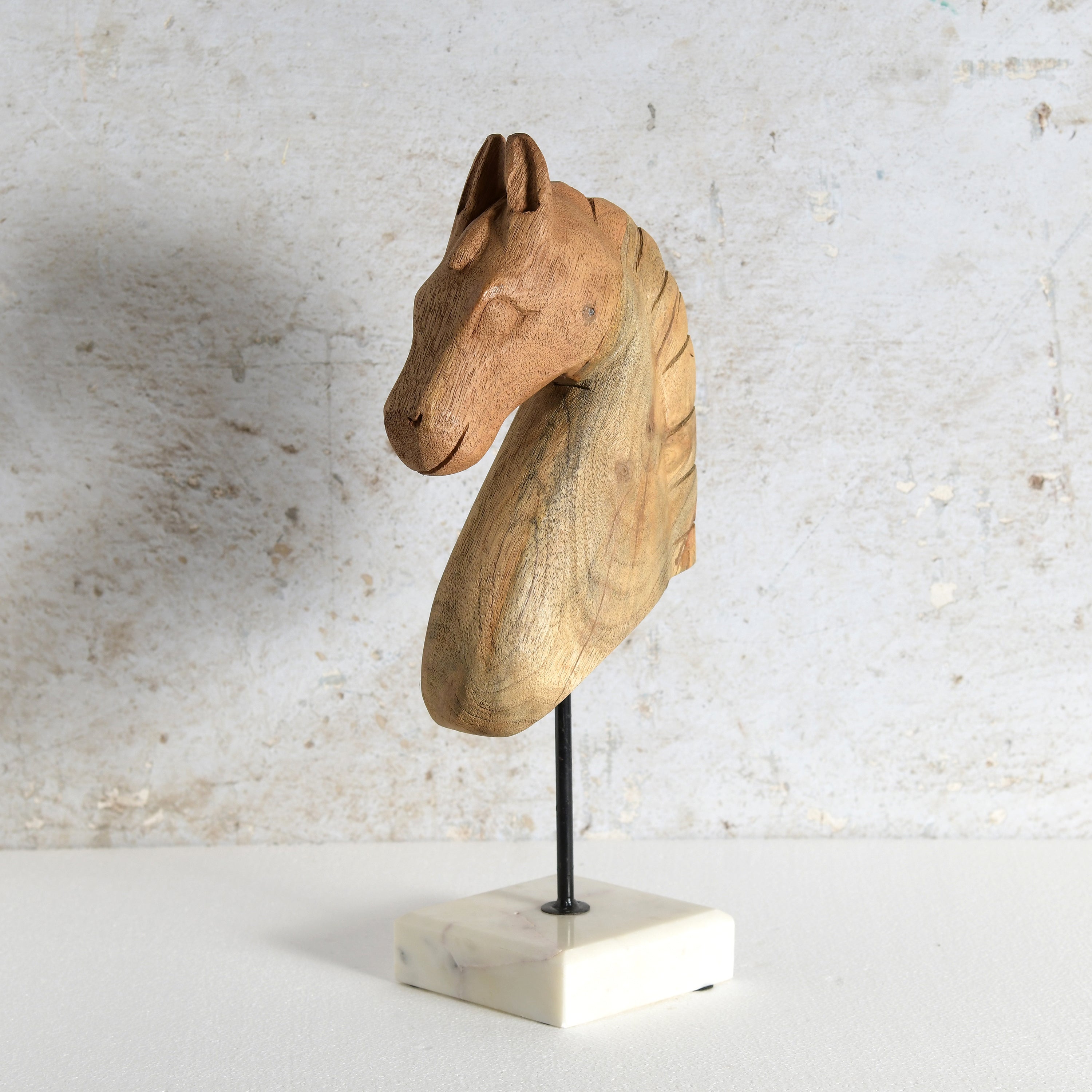 A carved wooden horse head sculpture mounted on a black metal rod over a white marble base.