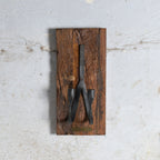 A vintage black metal two candle holder mounted on a rectangular rustic brown wooden plaque.