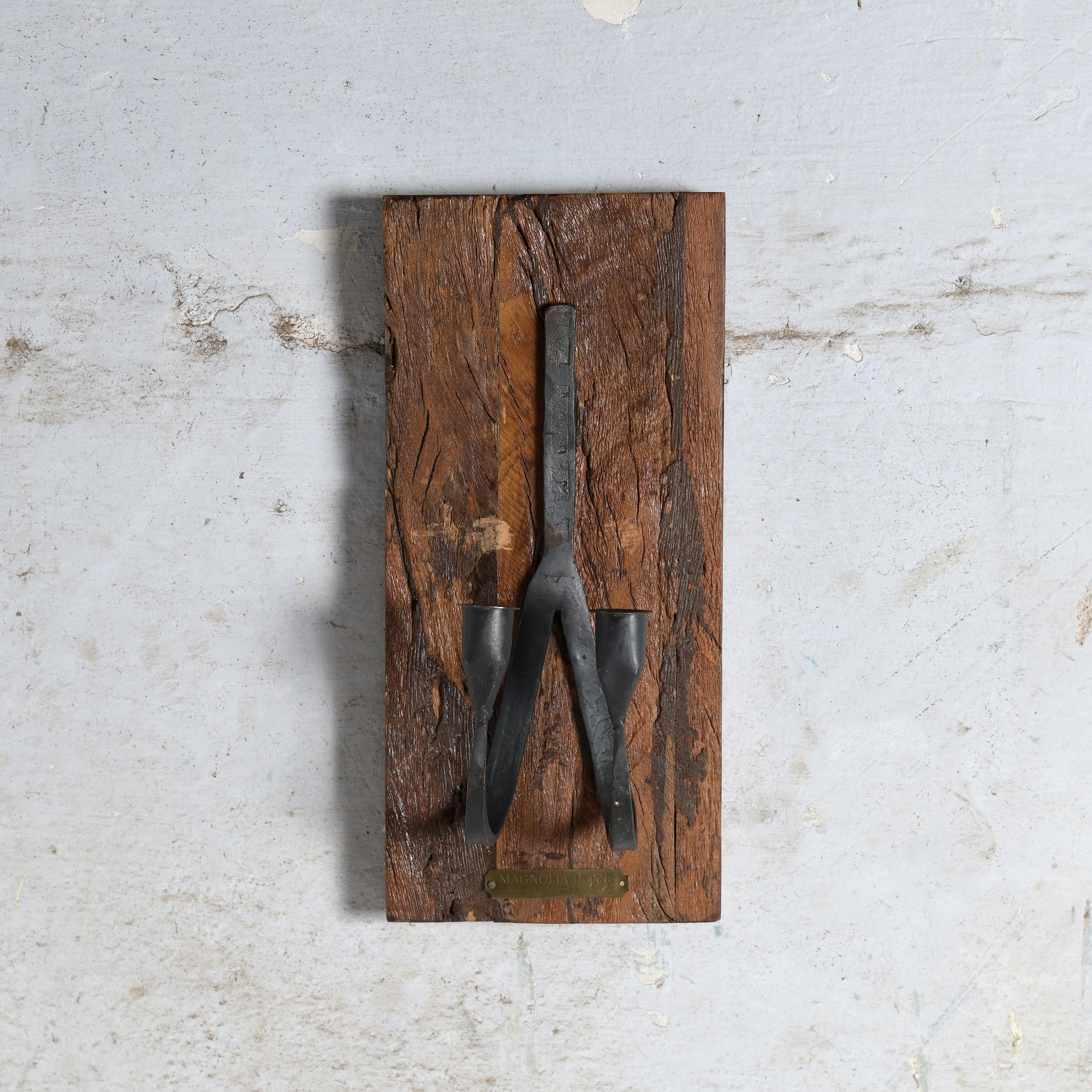 A vintage black metal two candle holder mounted on a rectangular rustic brown wooden plaque.