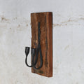 A rustic wall-mounted candle holder featuring a rectangular brown wooden plaque with two black metal candle holder.