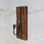 A rustic wall-mounted candle holder featuring a rectangular brown wooden plaque with two black metal candle holder.