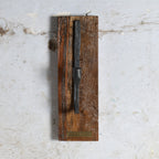 A vintage black metal candle holder mounted vertically on a rustic, rectangular brown wooden plaque.