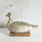 A distressed clay duck decor sculpture, mounted on a rustic wooden base.