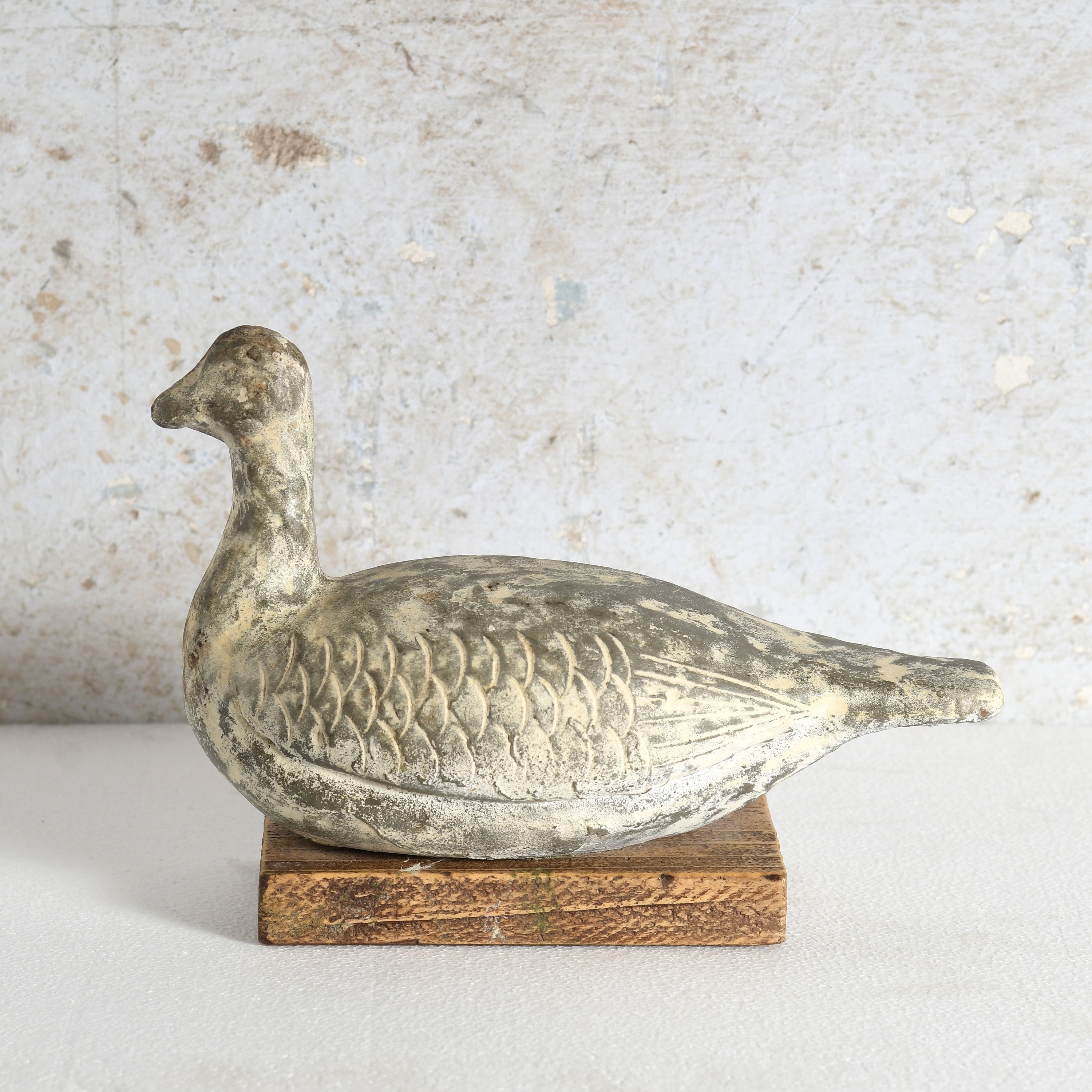 A distressed clay duck decor sculpture, mounted on a rustic wooden base.