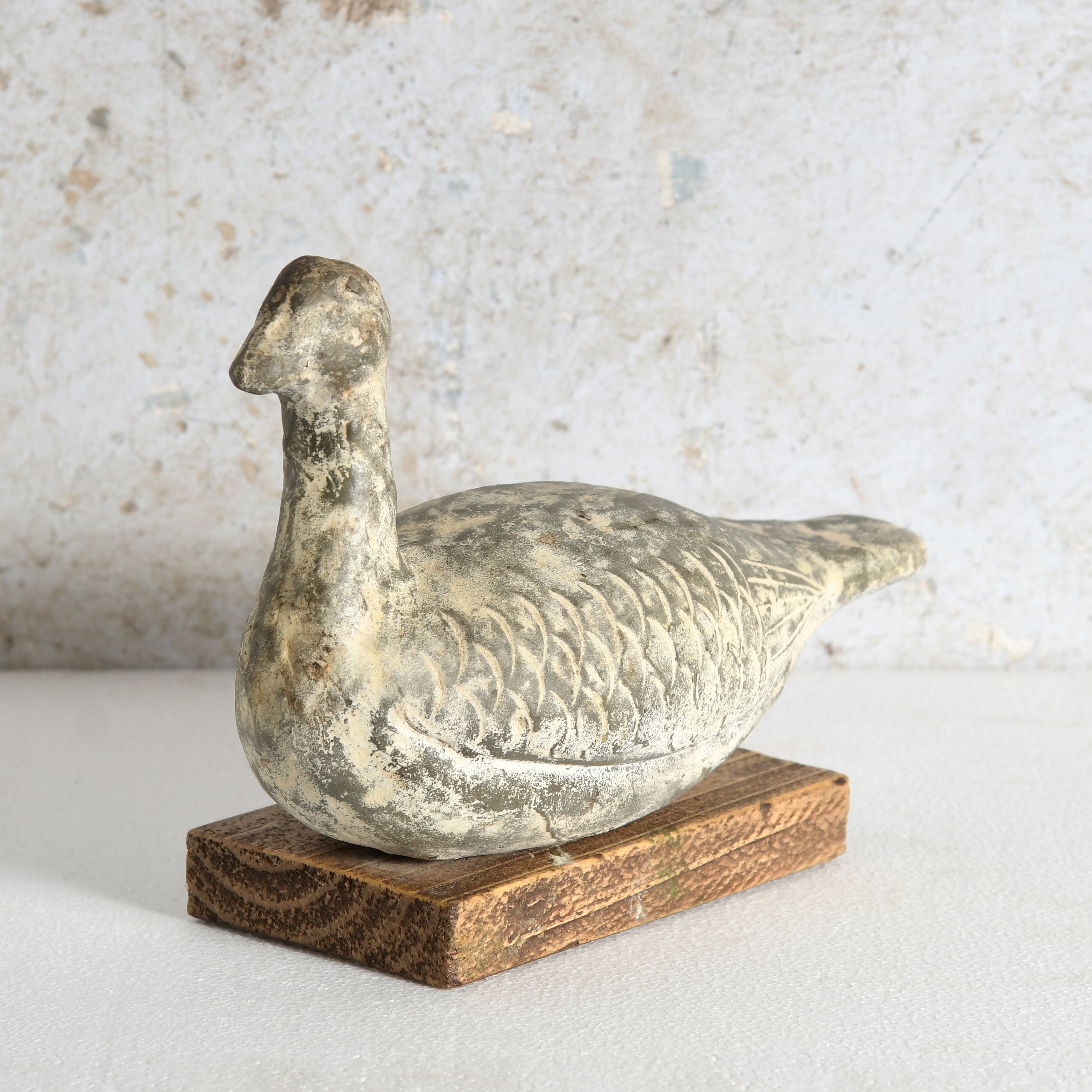 A distressed clay duck decor with a textured, weathered finish, mounted on a rustic rectangular wooden base.