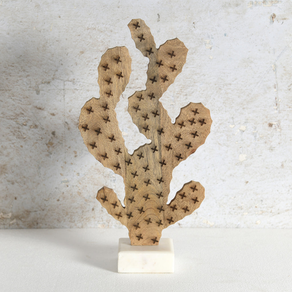 A decorative wooden cactus sculpture with laser-burned star details, mounted on a small white marble base against a textured light gray wall.