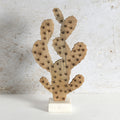 A decorative wooden cactus sculpture with laser-burned star details, mounted on a small white marble base against a textured light gray wall.