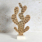 A decorative wooden cactus sculpture with laser-burned star details, mounted on a small white marble base against a textured light gray wall.