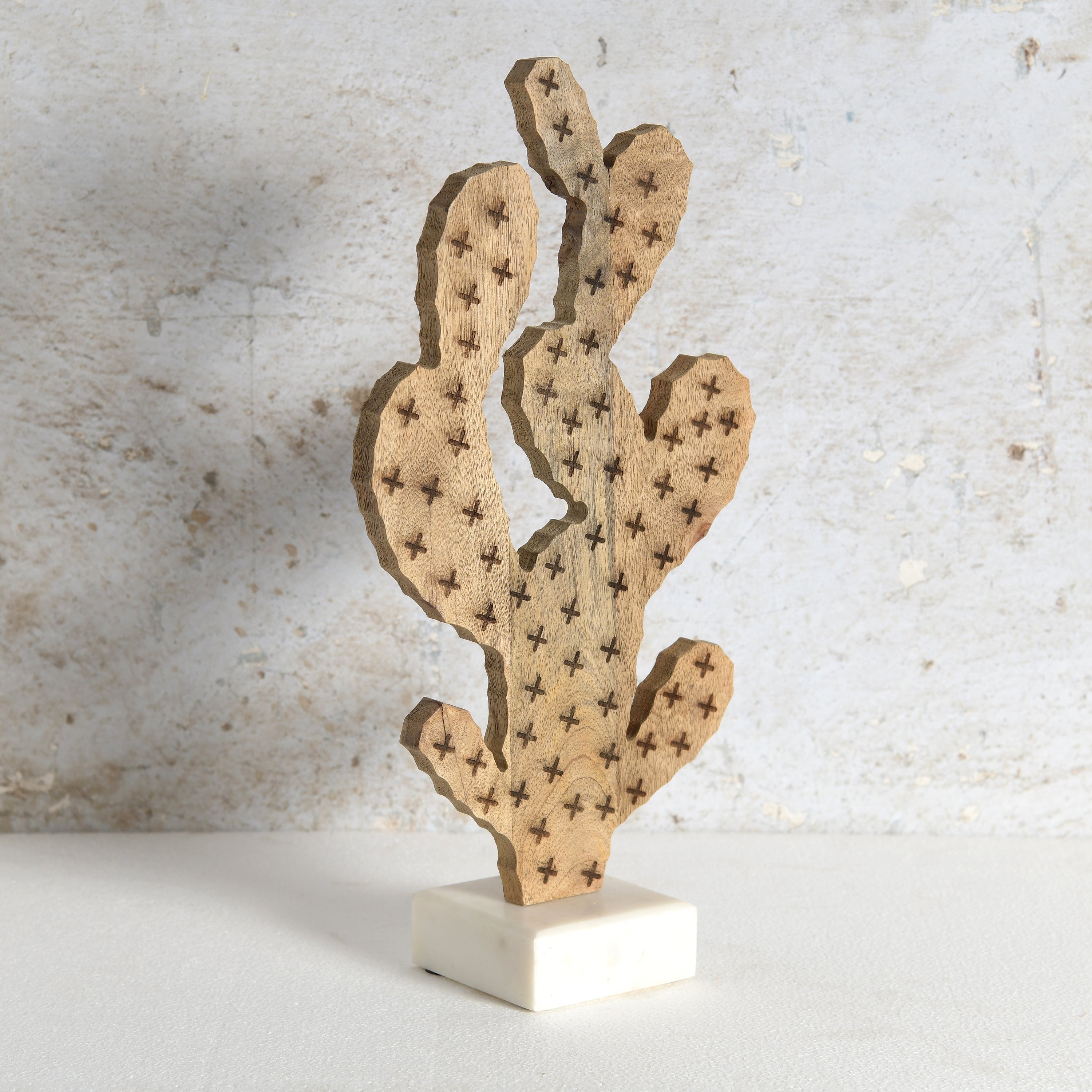 Decorative wooden cactus sculpture with visible star-shaped prickles, mounted on a white rectangular base,.