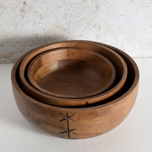 Three nested wooden bowls of varying sizes with a dark metal starburst accent on the front of the bowls.