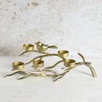 A brass candle holder shaped like a branch with a small bird perched on it, featuring five candle cups.
