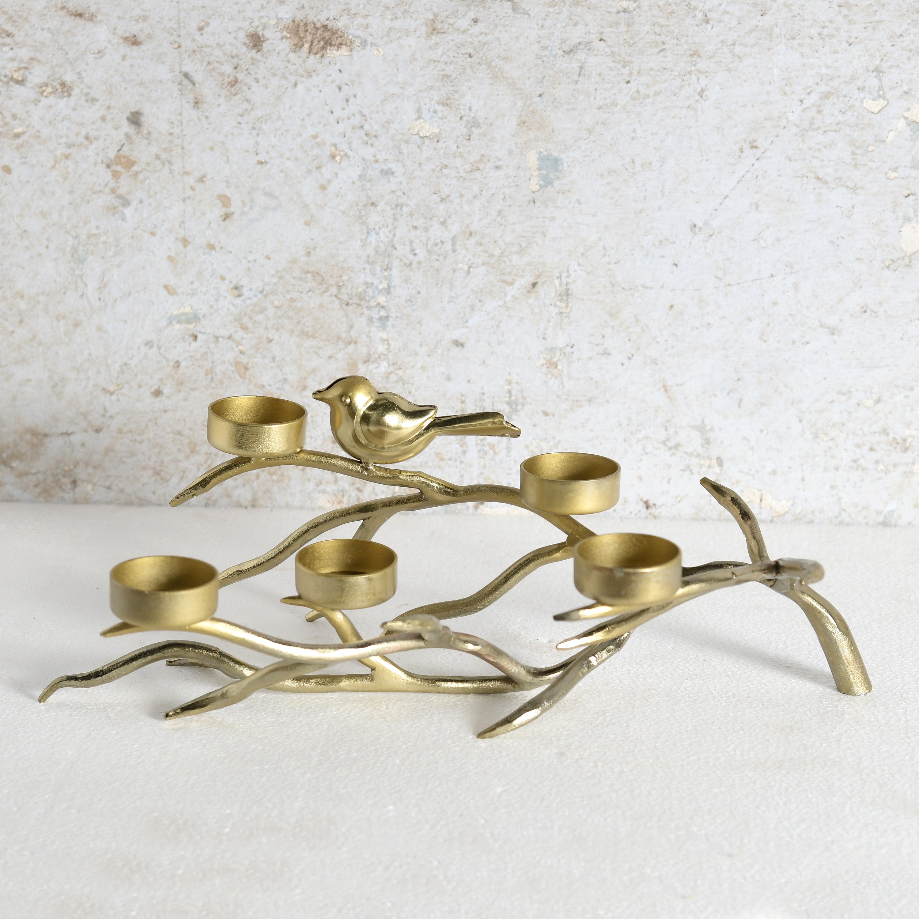 A brass candle holder shaped like a branch with a small bird perched on it, featuring five candle cups.