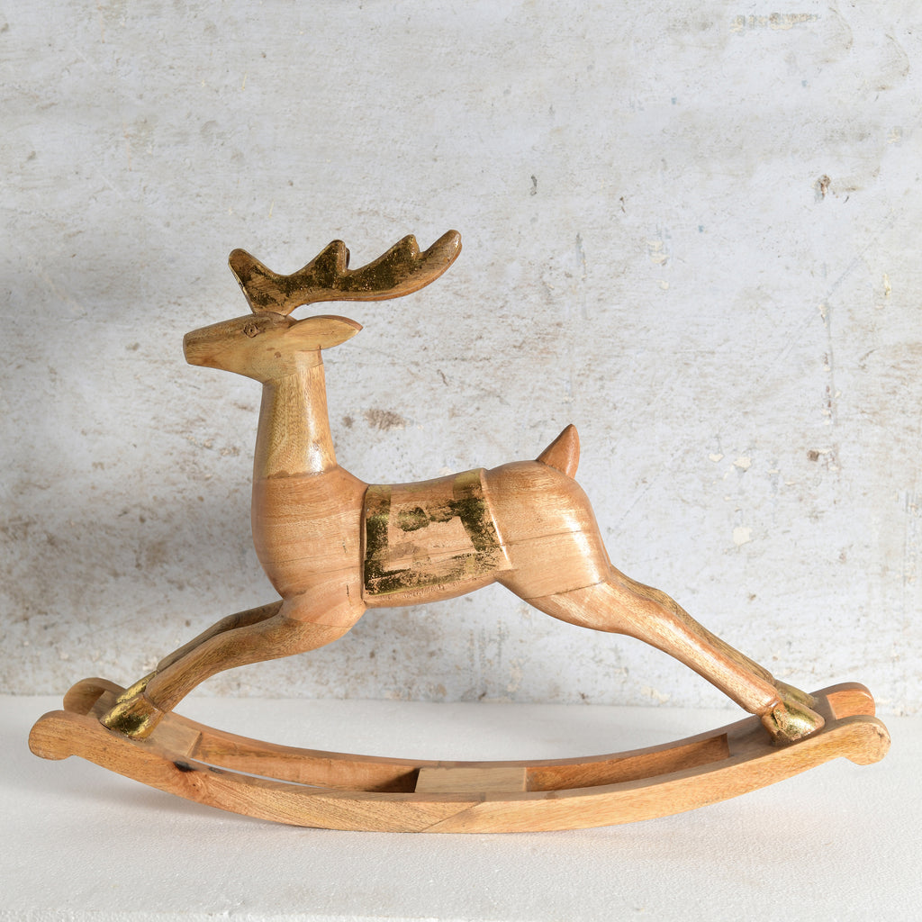 A handcrafted wooden rocking deer toy with gold-painted accents on the antlers, hooves, and side details.