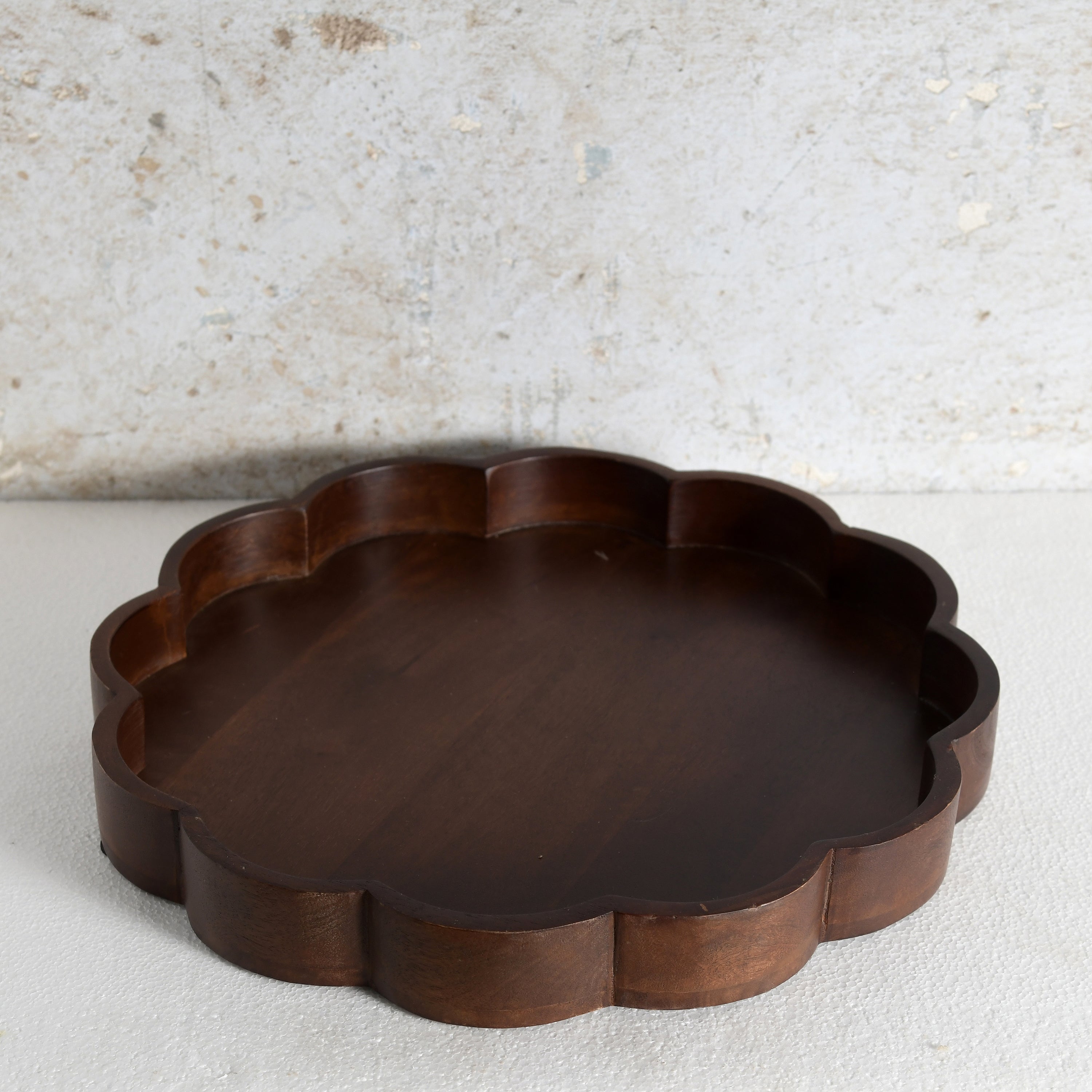 A scalloped-edge wooden tray in a dark brown finish. 