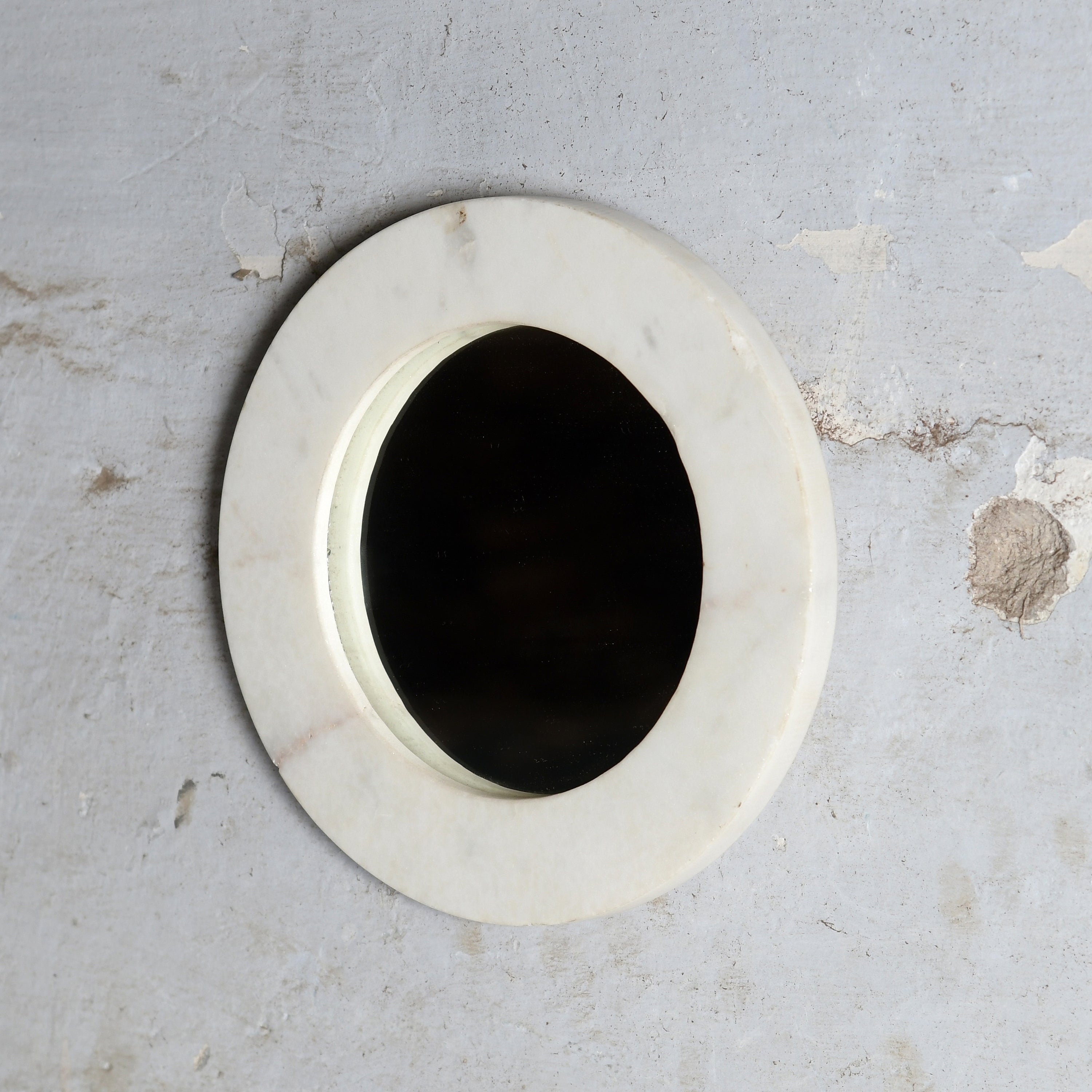 A round white marble wall mirror with a thick white frame.