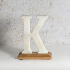 A freestanding decorative letter K made of marble, mounted on a rectangular light brown wooden base.
