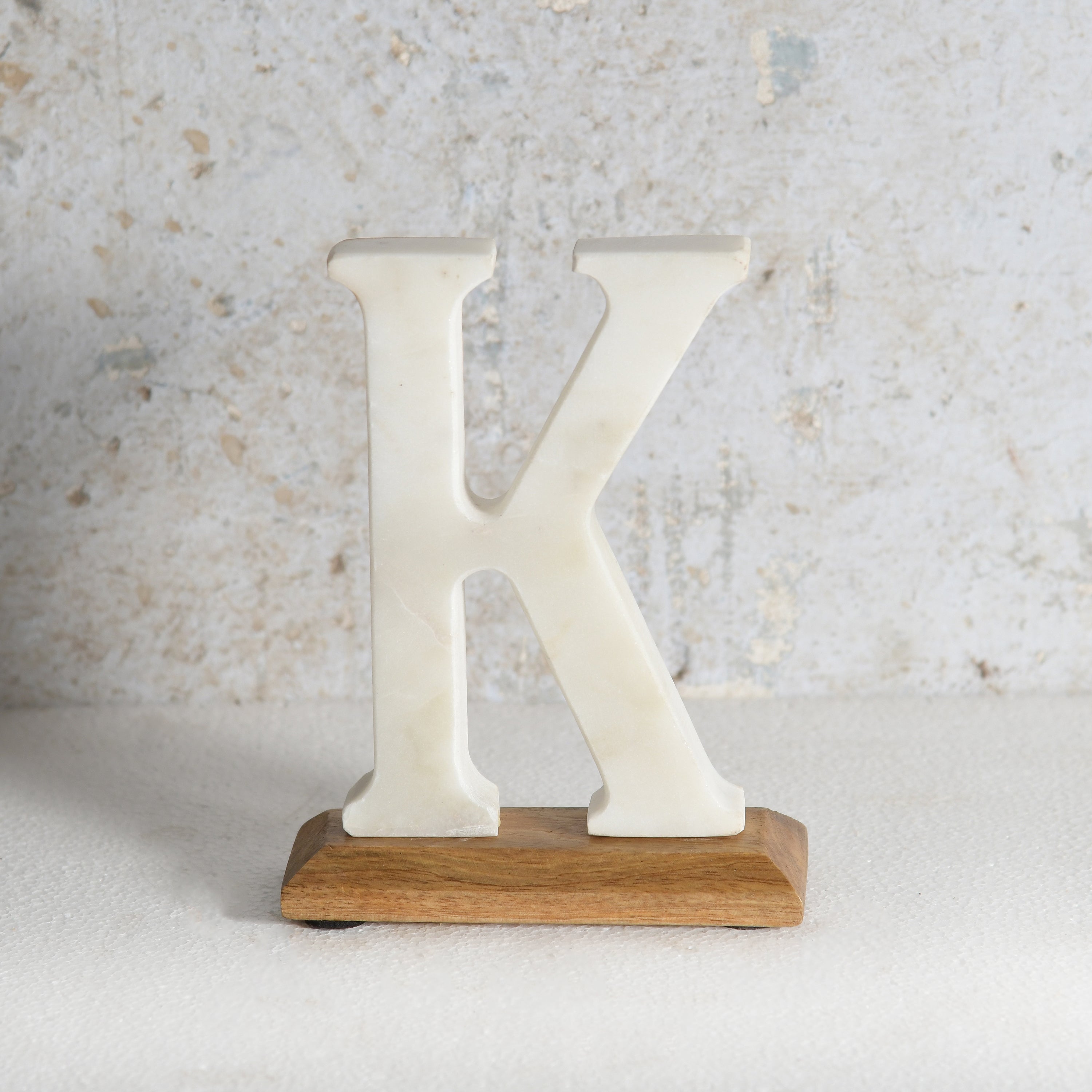 A freestanding decorative letter K made of marble, mounted on a rectangular light brown wooden base.