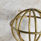 A close-up of a metallic gold wireframe decorative sphere against a textured off-white background.